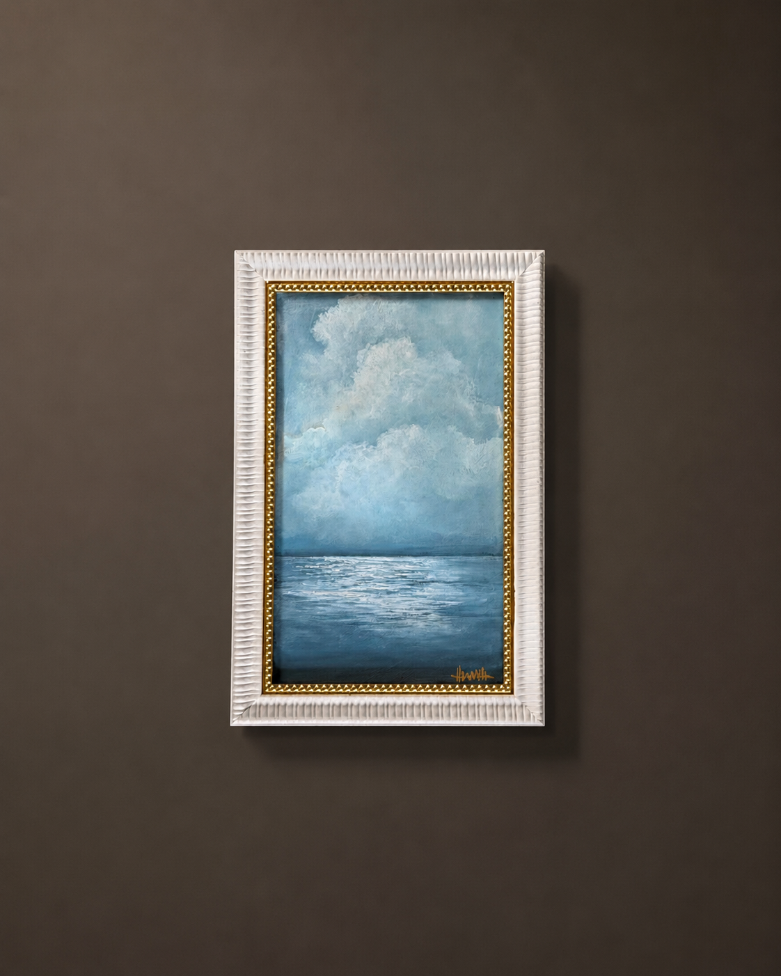 A framed vertical painting of a blue ocean under a cloudy sky, displayed on a dark brown wall. The painting features a textured white frame with a gold inner border.