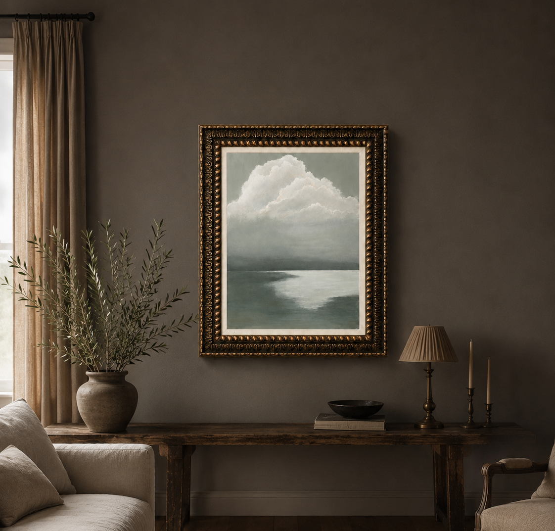 A framed landscape painting of a cloudy sea under a bright sky, displayed on a dark gray wall in a styled living room with a console table, lamp, and sofa.