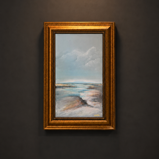 A framed landscape painting of a beach or salt flat under a cloudy sky, in a wide ornate gold frame, mounted on a dark gray wall.